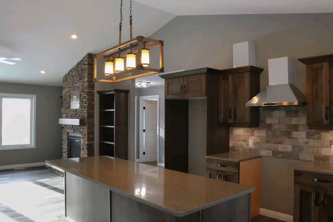 Modern kitchen with a stone fireplace wall, an island with a granite countertop, and a wooden pendant light. Warm tones create a welcoming atmosphere.