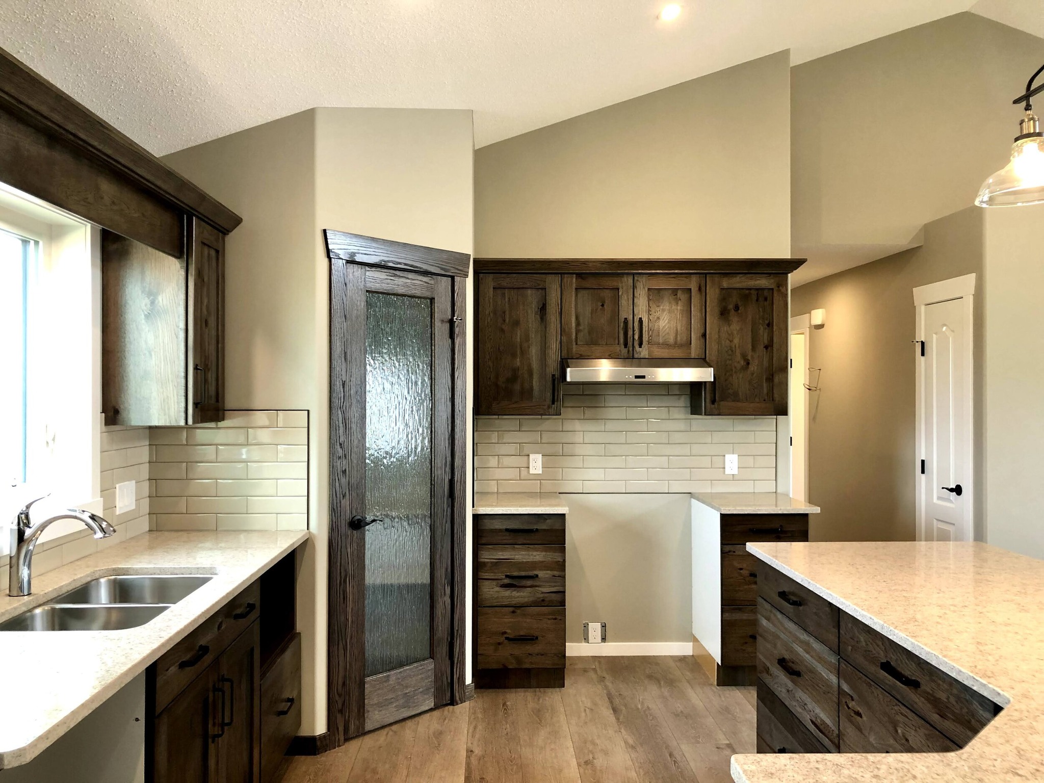 A modern kitchen with wood cabinets, cream countertops, subway tile backsplash, stainless steel sink, and range hood. Warm, inviting tones and soft lighting.