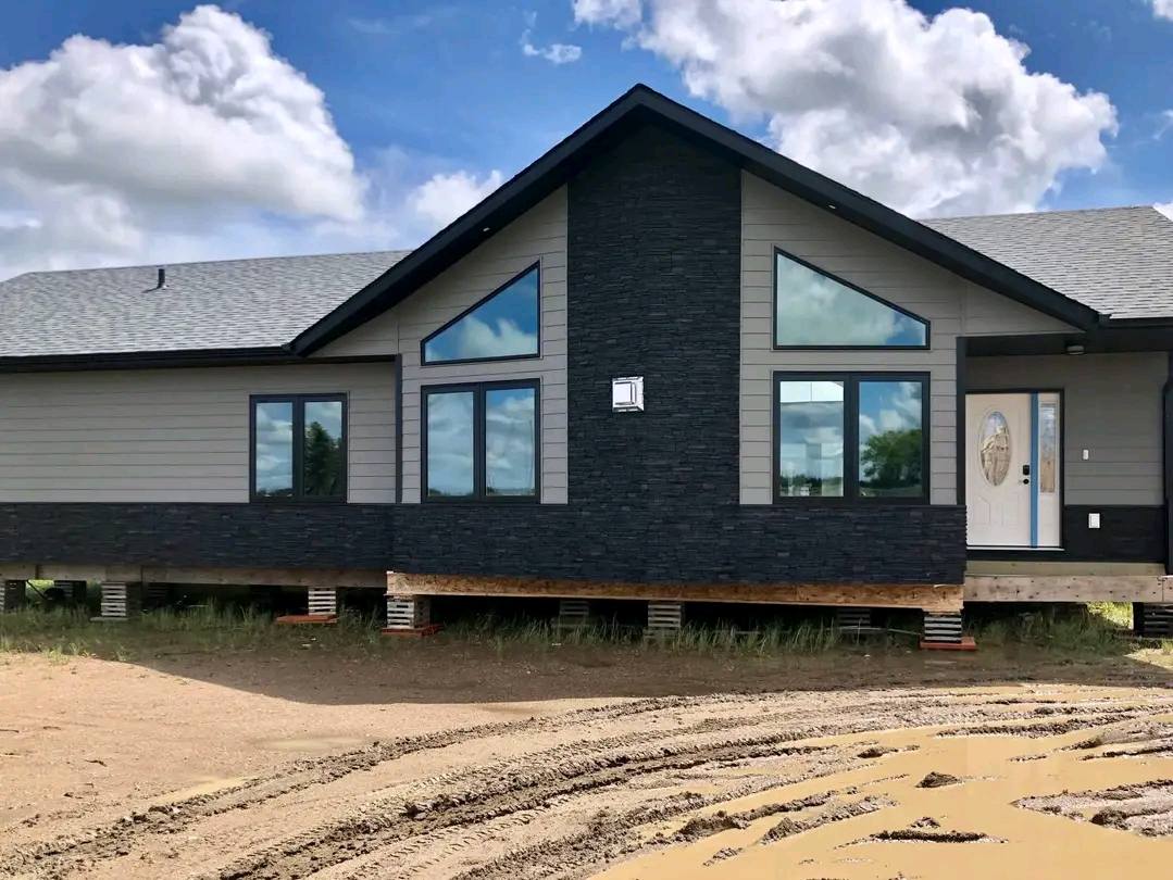 A modern, elevated house with a black-and-gray facade under a blue sky with clouds. Large windows and a decorative front door add elegance.