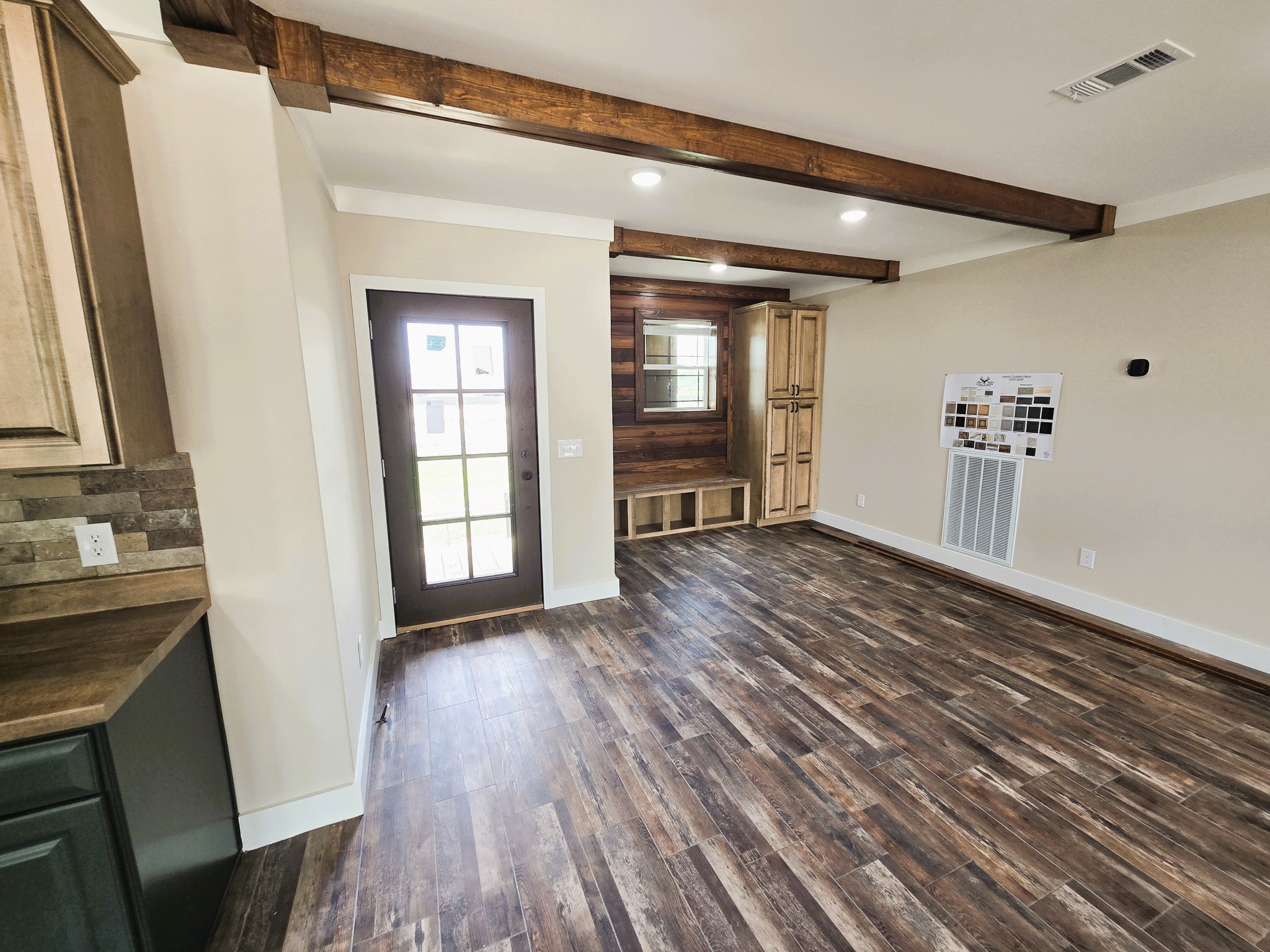 Warm and rustic room featuring dark wooden beams, polished wood flooring, and a glass-paneled door. Calming tones create inviting ambiance.