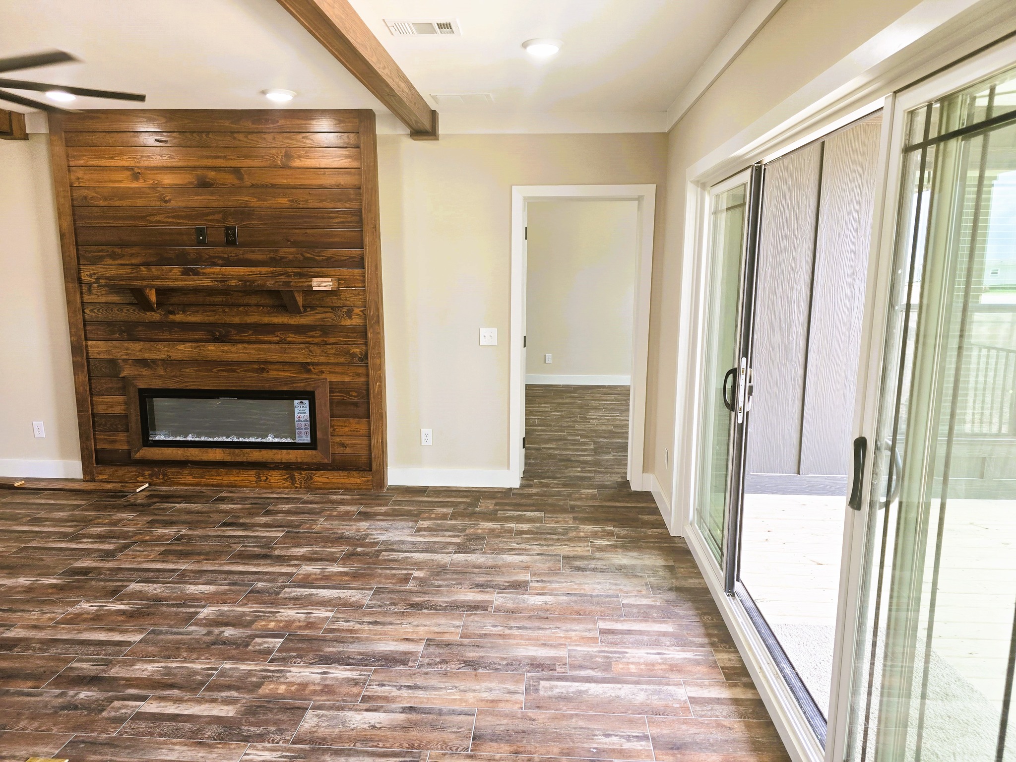 Spacious room with wood-paneled accent wall and electric fireplace, sliding glass doors, and wooden flooring, evoking a warm, inviting atmosphere.