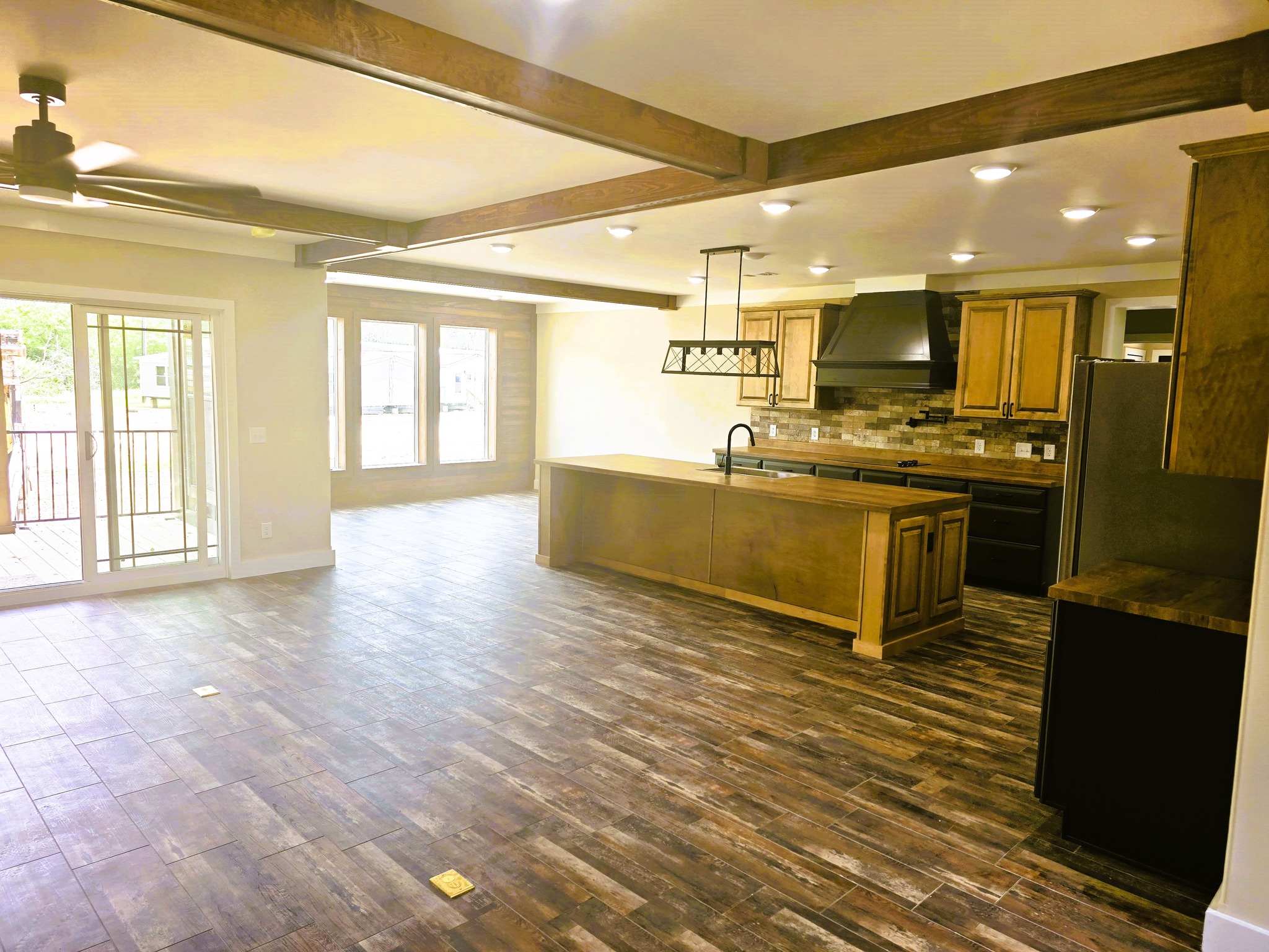 Spacious kitchen and dining area with wooden flooring, ceiling beams, and modern light fixtures. Large windows and sliding doors provide natural light.