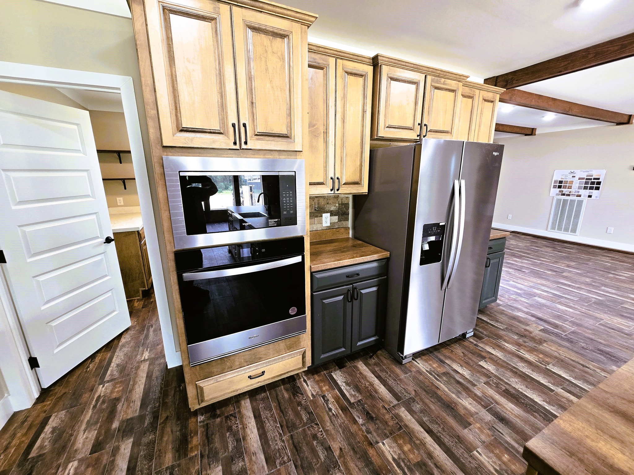 Modern kitchen with light wood cabinets, stainless steel oven, and fridge. Dark wood flooring and ceiling beams add a rustic yet contemporary feel.