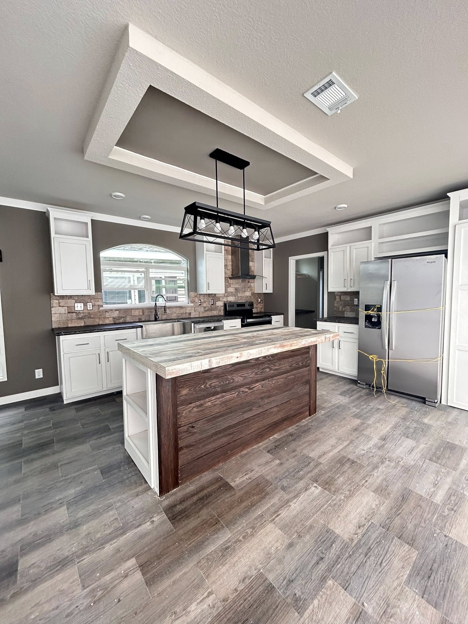 Modern kitchen with a rustic island, light wood floors, white cabinets, stainless steel appliances, and brown tile backsplash. Bright, inviting ambiance.