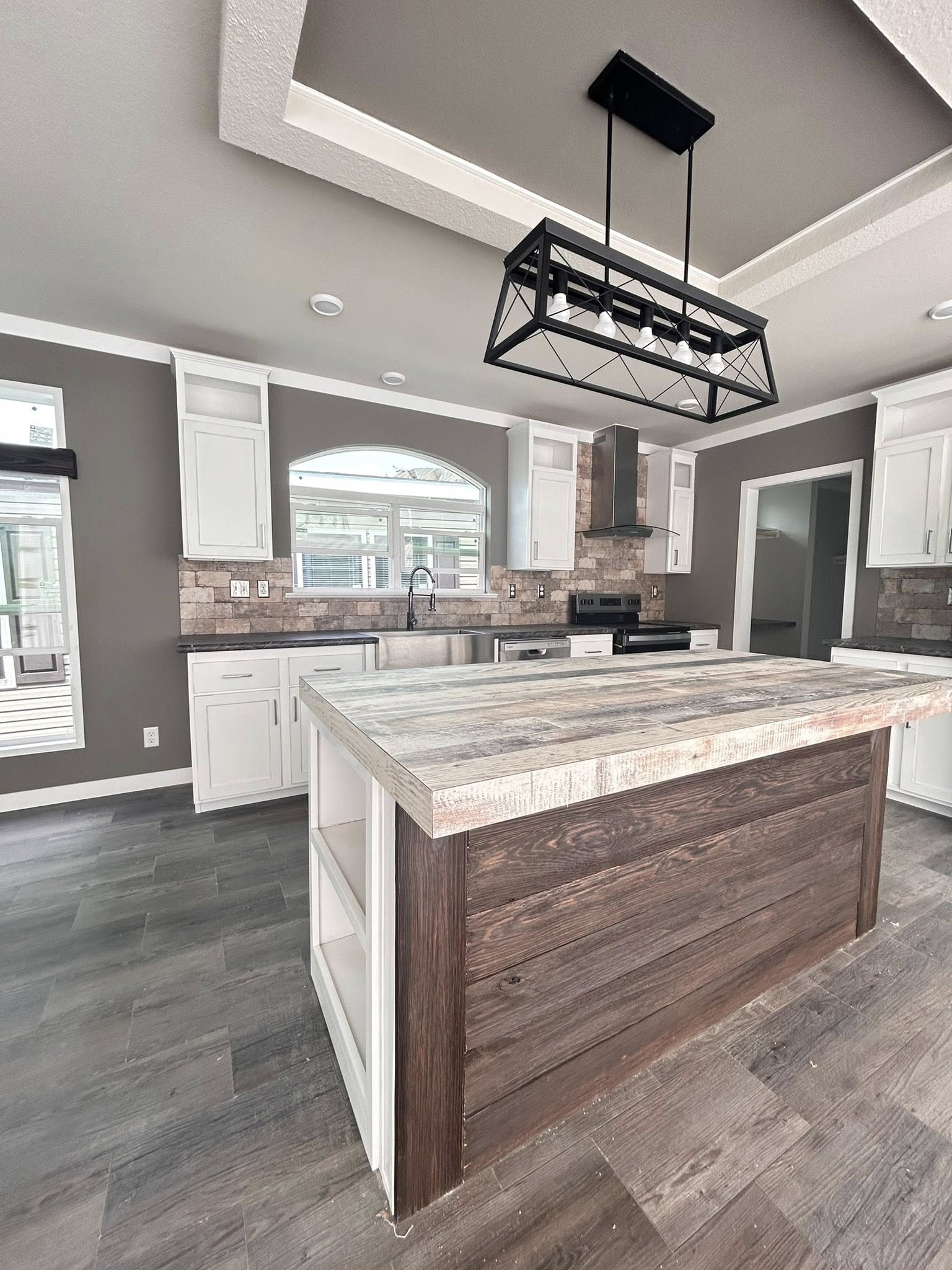 Modern kitchen with a rustic island featuring a wood finish and open shelving. White cabinets, stainless steel appliances, and a geometric light fixture.