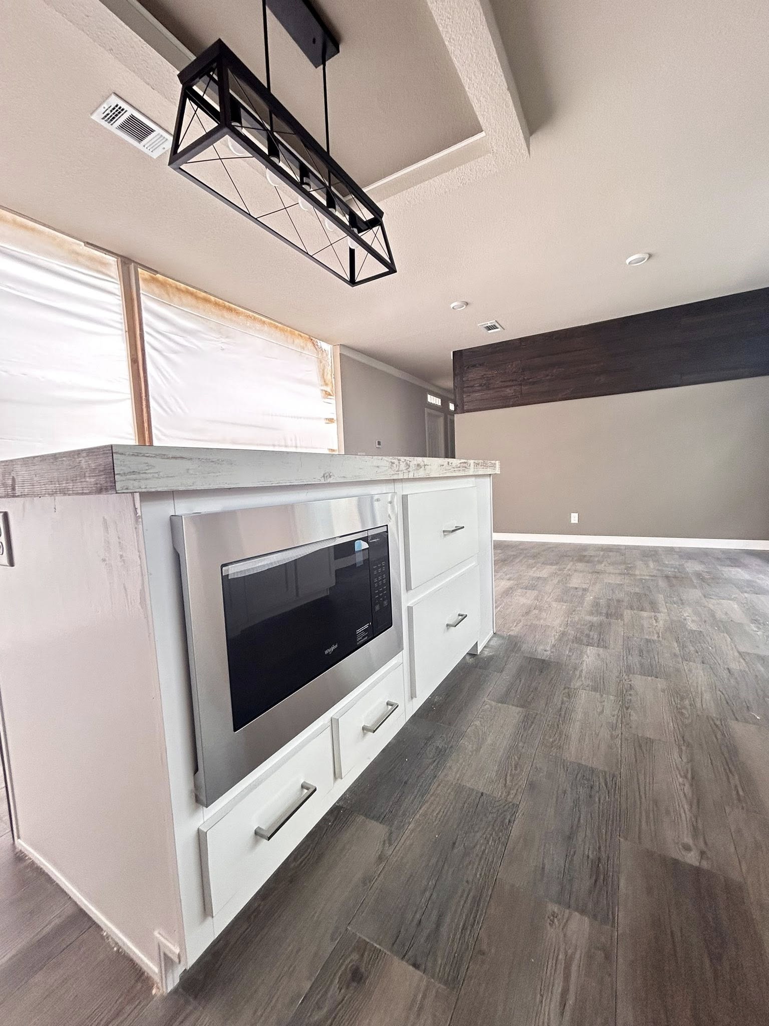 Modern kitchen with light wood flooring, a white island featuring built-in microwave, and black rectangular pendant light. Bright, calm, and minimalist.