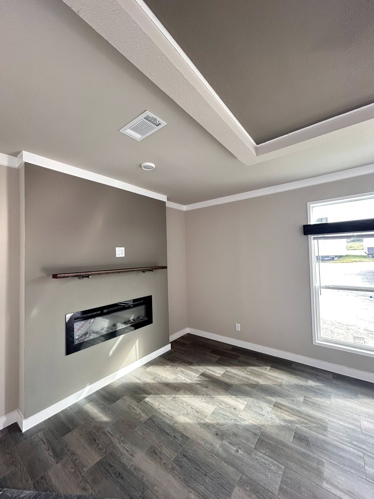 Modern room with gray walls, recessed ceiling, and vinyl flooring. Features a wall-mounted fireplace and large window illuminating the space naturally.