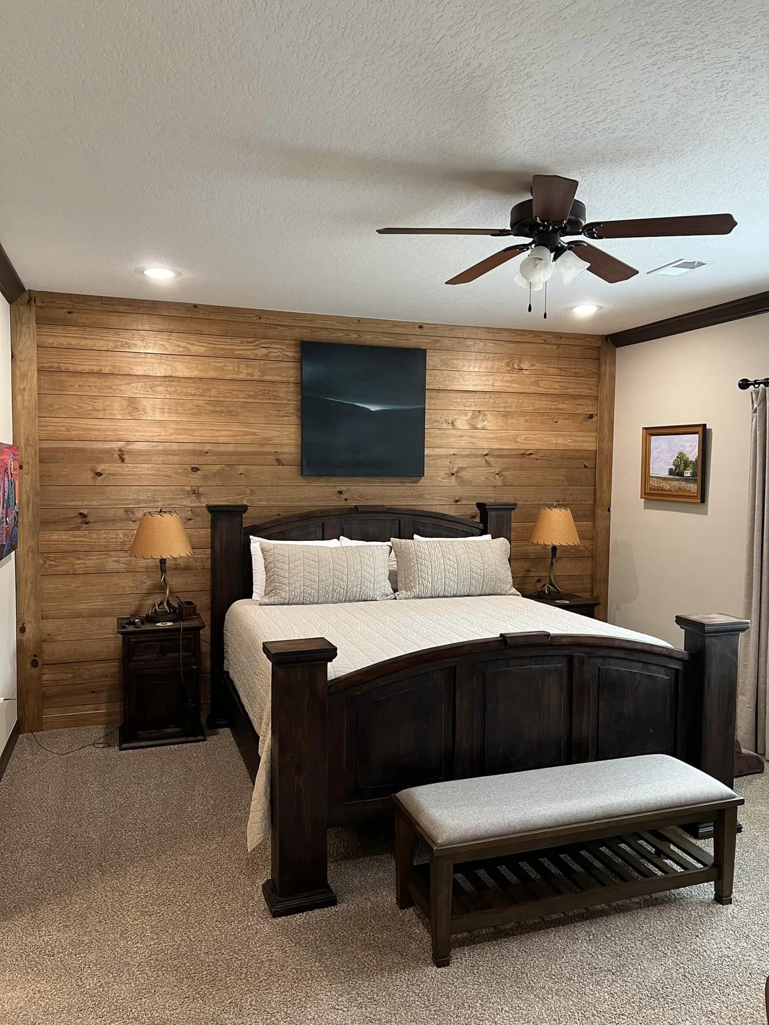 Warm, rustic dining room with a long wooden table and chairs set for twelve. Wooden beams, cozy lighting, and wall art enhance the inviting atmosphere.