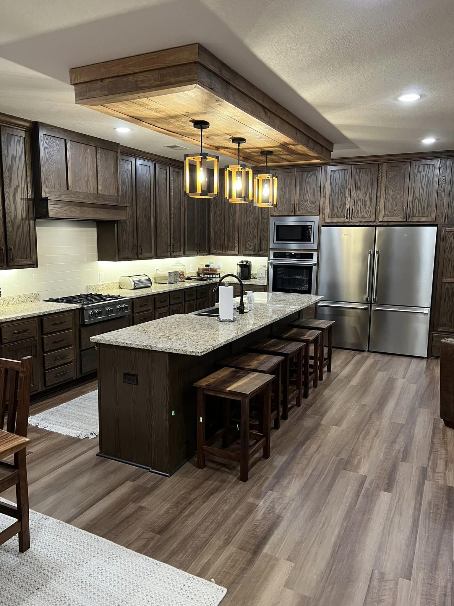 Spacious kitchen with dark wood cabinets, stainless steel appliances, and an island featuring bar stools and pendant lights, creating a warm, inviting atmosphere.