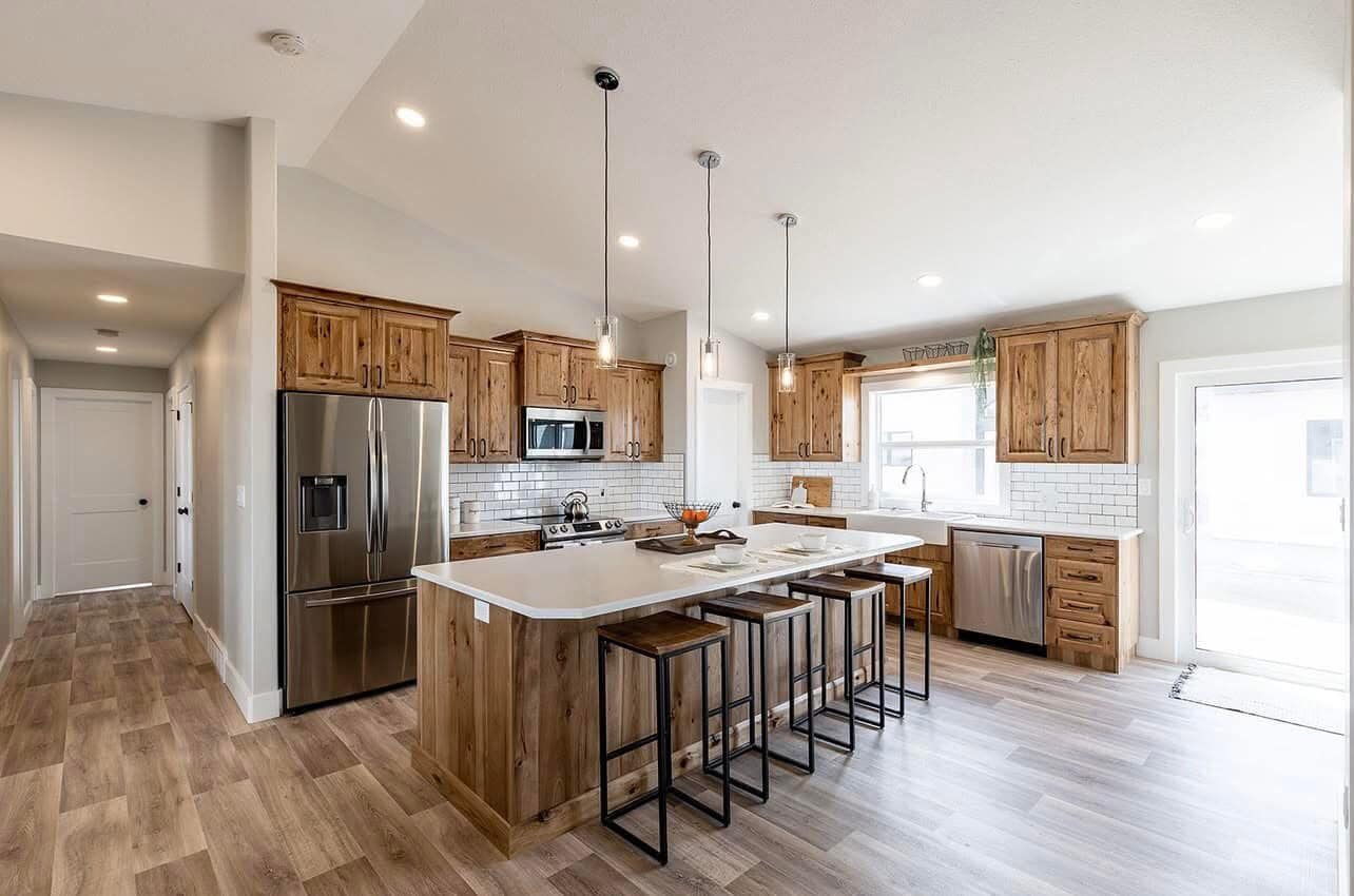 Spacious kitchen with light wood cabinets and flooring. Features a large island with white countertop, modern appliances, and three pendant lights, conveying a warm and inviting atmosphere.