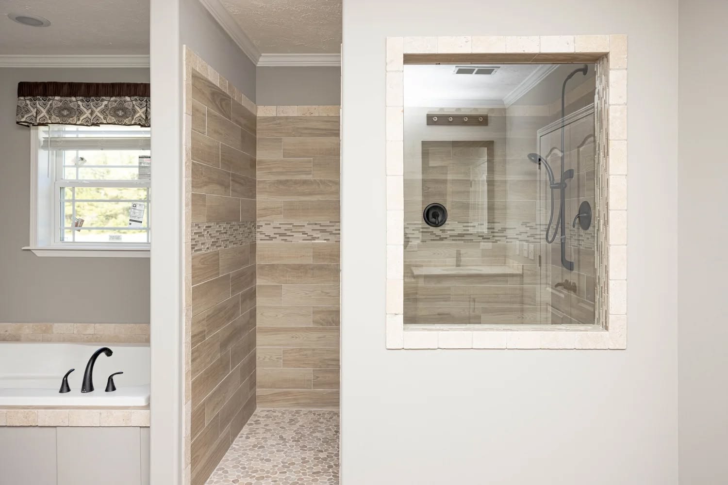 Modern bathroom showcasing a glass-enclosed shower and a bathtub with black fixtures. Beige tiles and natural light create a calming, sleek atmosphere.