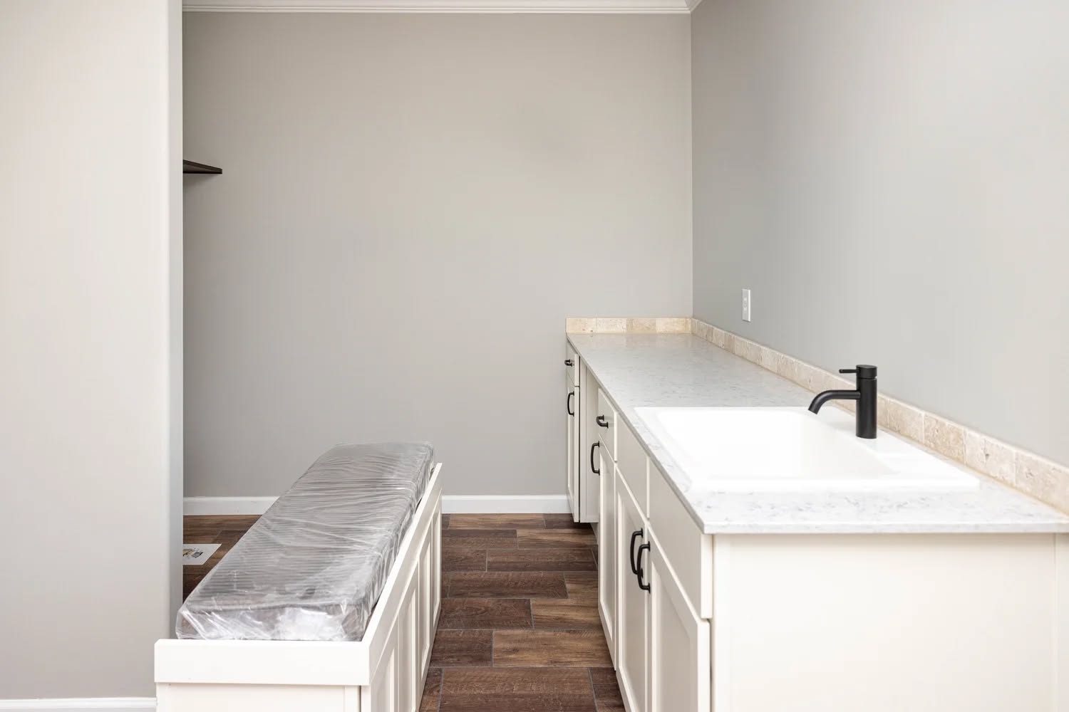 Minimalist laundry room with light gray walls, white cabinetry, a marble countertop, and a black faucet. Dark wood floors add contrast. Quiet elegance.