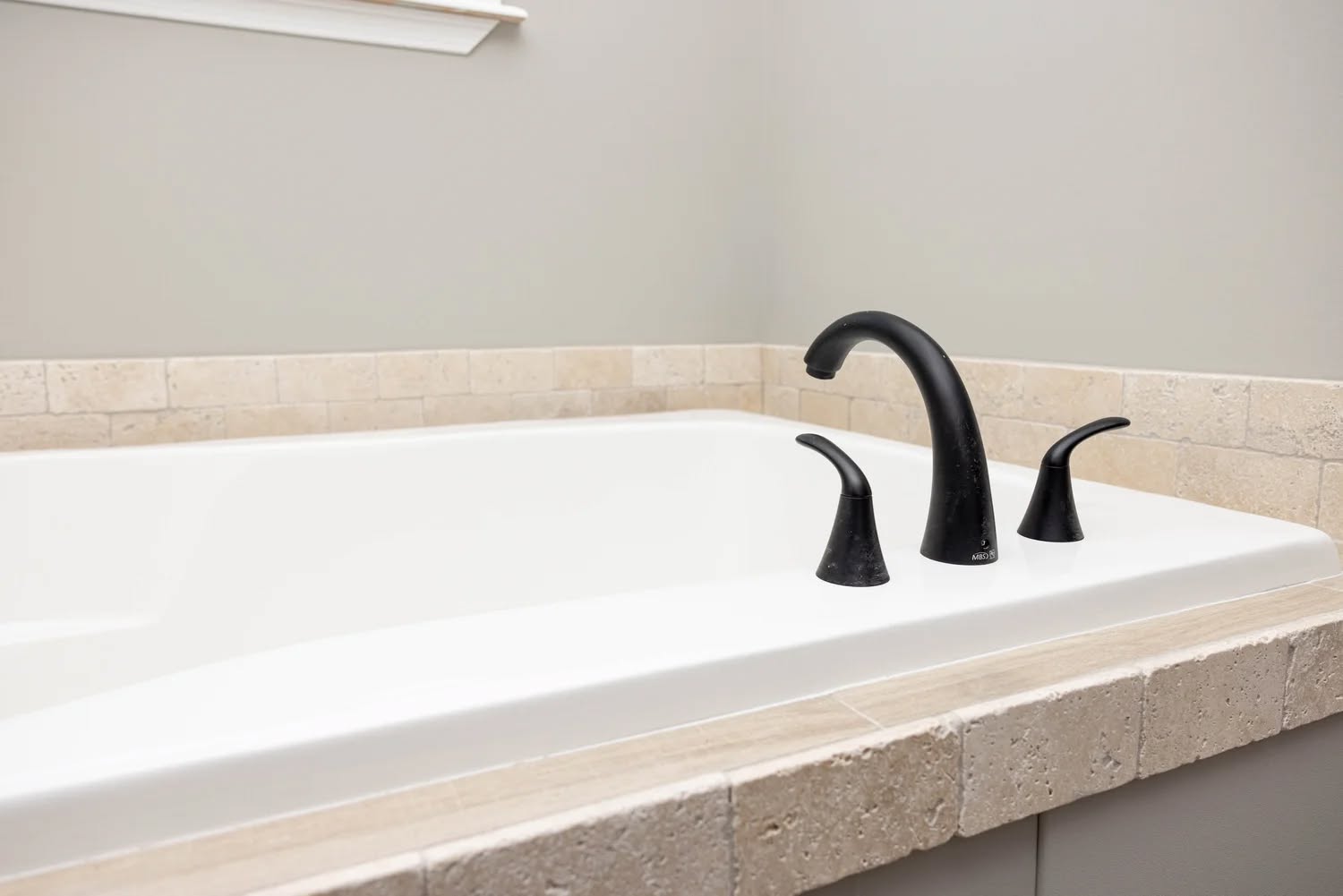 A white bathtub with beige tile surround, featuring matte black faucet handles and spout. The space appears minimalist and modern.