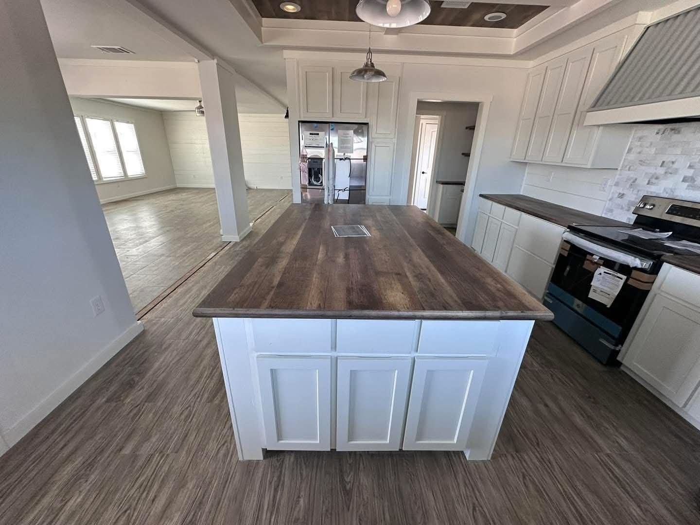 Modern kitchen with large wooden island, white cabinets, and stainless steel appliances. Bright, open layout with light wood floors.