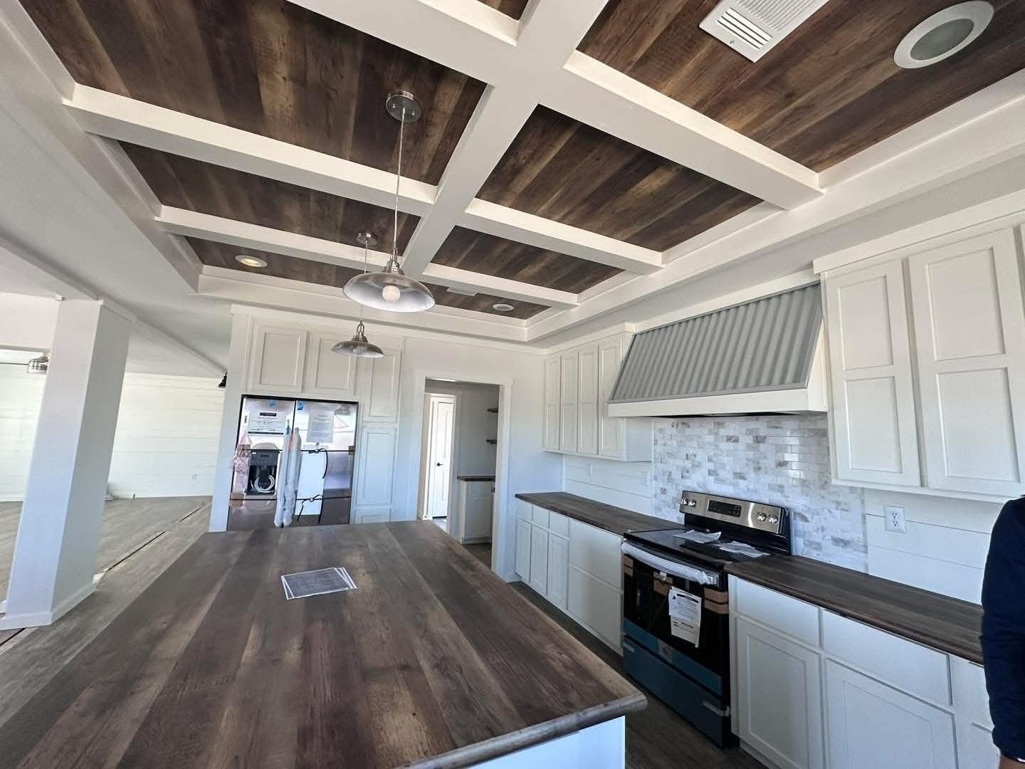 Spacious modern kitchen with wooden coffered ceiling and matching countertops. White cabinetry, stainless steel appliances, and pendant lighting. Clean and elegant design.