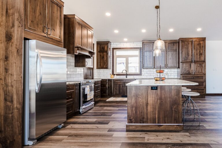 Spacious kitchen with dark wood cabinets, white subway tiles, and stainless steel appliances. Warm lighting, large island with pendant lights. Cozy and inviting.
