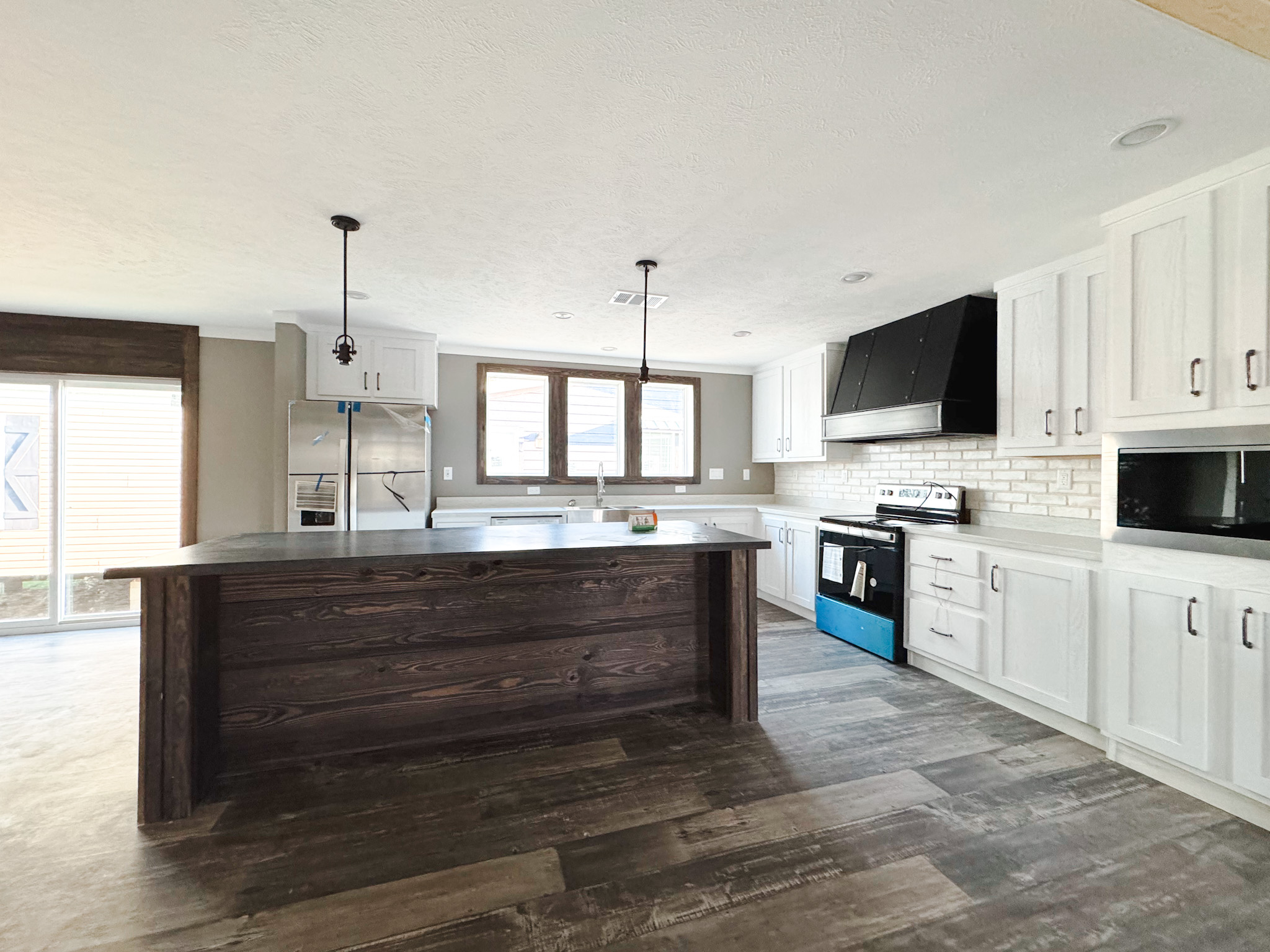 Modern kitchen with white cabinets, dark wood island, stainless steel appliances, and a brick backsplash. Features pendant lights and large windows. Cozy and inviting atmosphere.