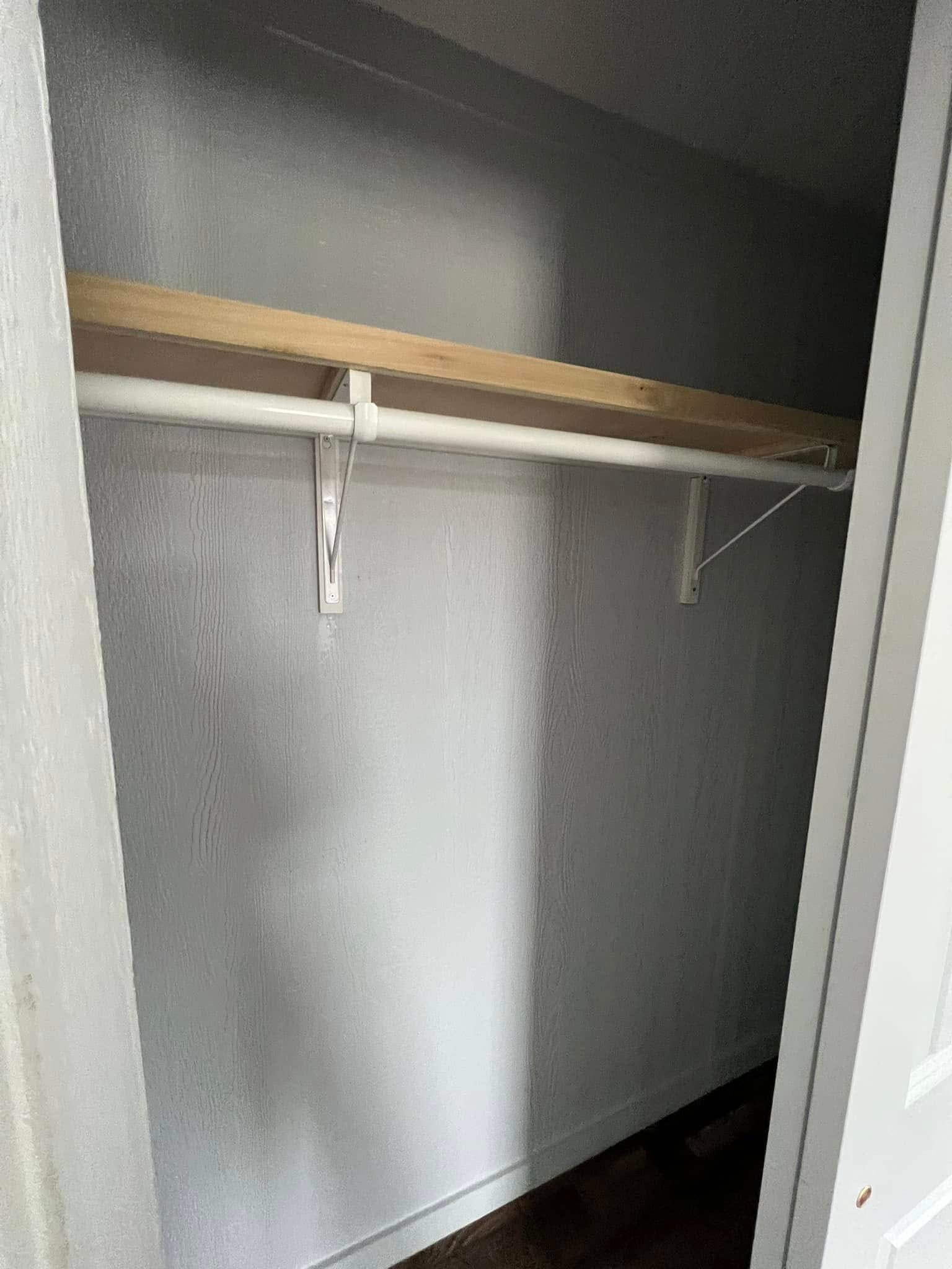 Empty white closet with a wooden shelf above a white metal clothes rod. Minimalistic and clean, the space appears freshly painted.