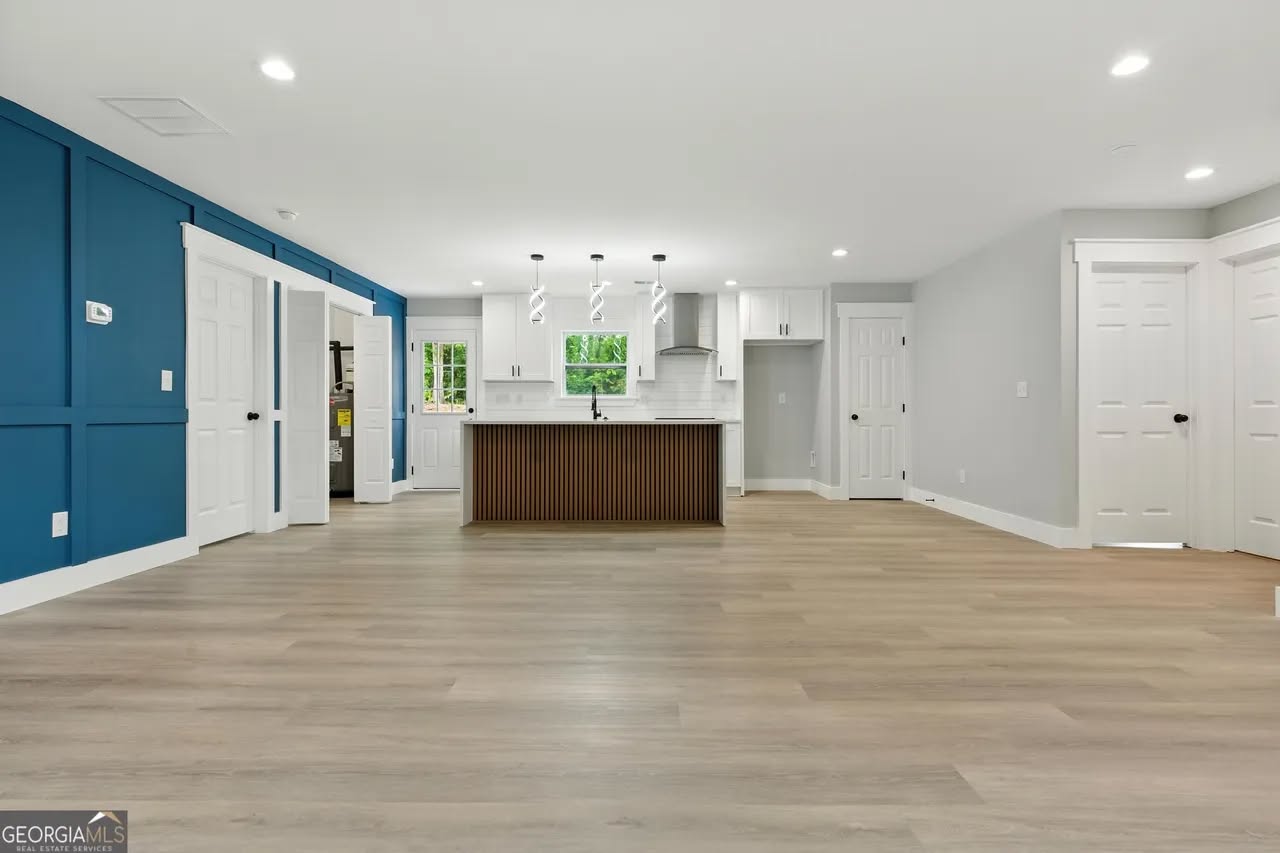 Spacious, modern kitchen and living area with wooden flooring and a bold blue accent wall. Central island features pendant lighting and white cabinetry.