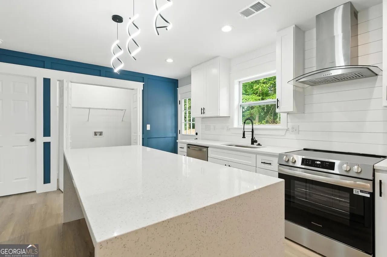 Modern kitchen with white countertops, sleek cabinetry, and a stainless steel oven and range hood. A bold blue accent wall adds contrast.