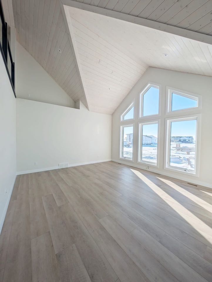Spacious, sunlit room with vaulted ceiling, large triangular windows showing snowy landscape. Light wood floors and minimalist white walls convey tranquility.