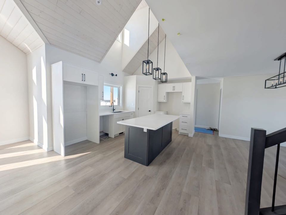 Spacious modern kitchen with high ceilings, white cabinets, a dark island, and light wood flooring. Pendant lights add elegance and warmth.