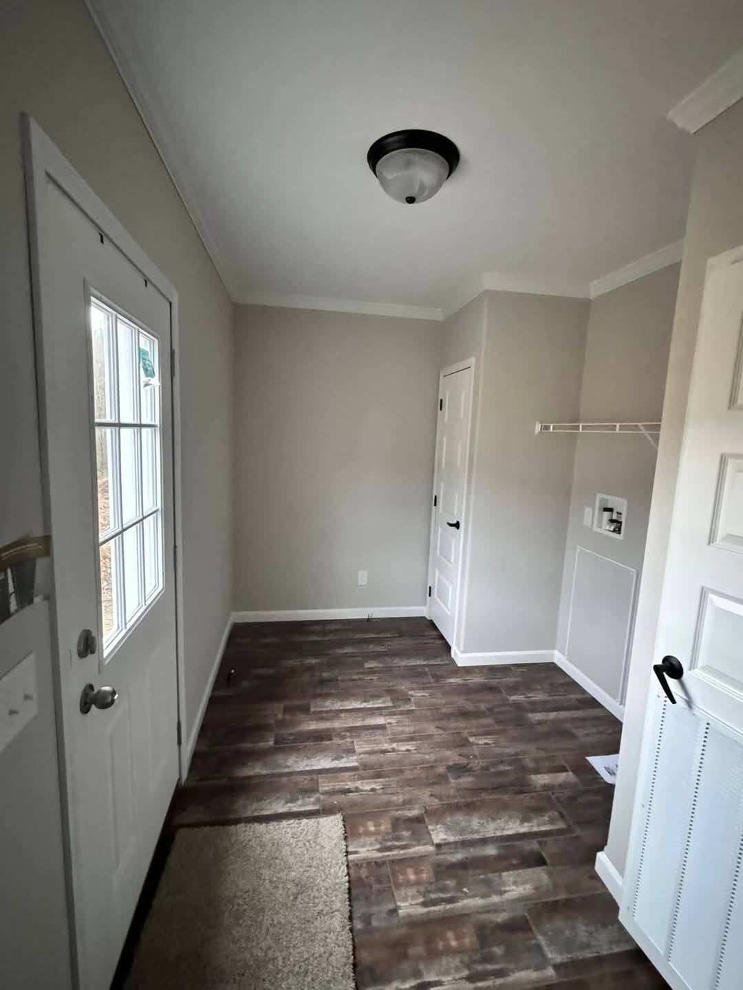 Narrow laundry room with wood-look flooring, gray walls, and white trim. A door with windows on the left and a shelf on the right create a clean, functional space.