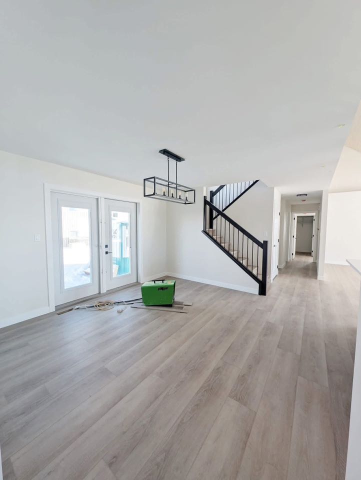 Spacious, unfurnished room with light wood flooring, white walls, a modern black staircase, and glass double doors leading outside. Bright and airy feel.