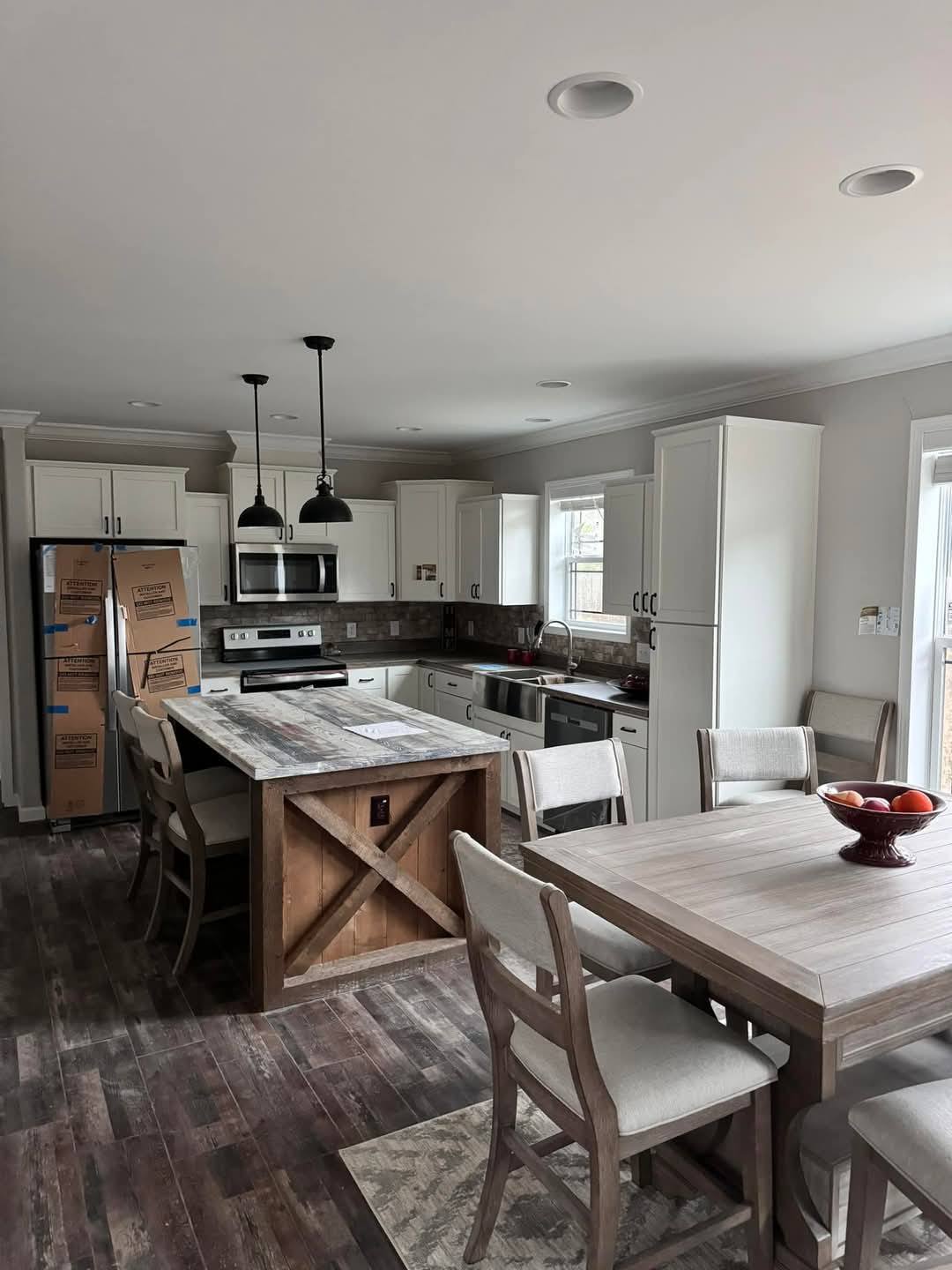 Modern kitchen with light gray cabinets, wooden island, and dining table on dark wood floors. Stainless steel appliances and pendant lights add elegance.