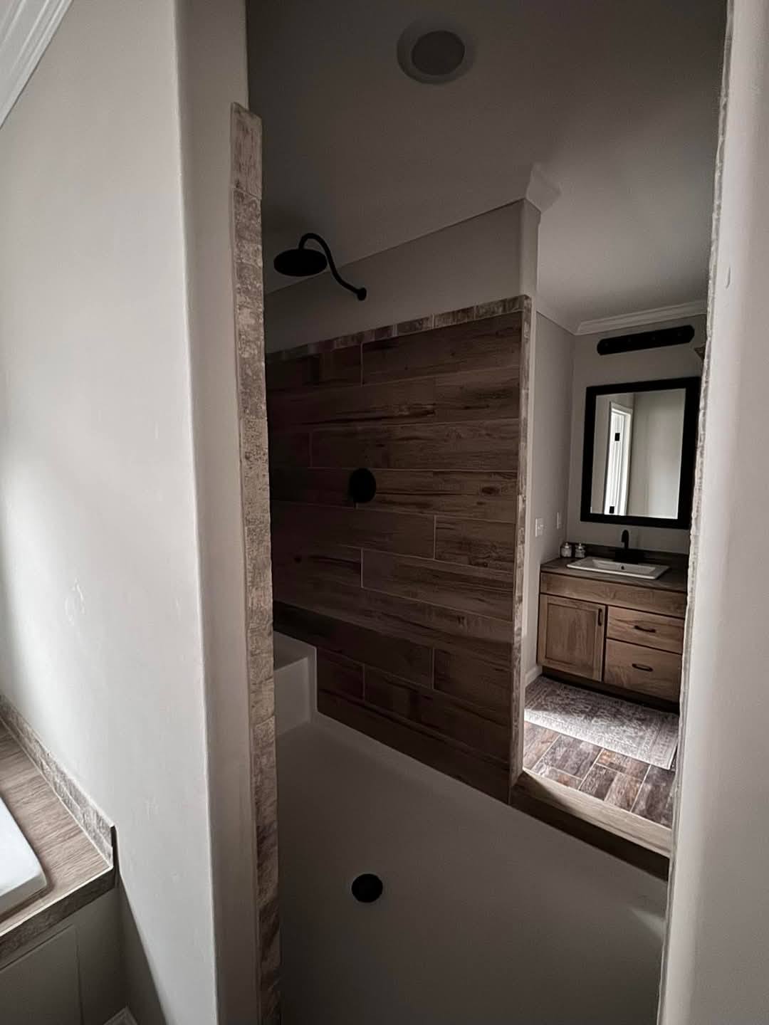 Modern bathroom with dark wood tiles, a walk-in shower, black showerhead, and a wooden vanity with a mirror. The atmosphere is cozy and elegant.