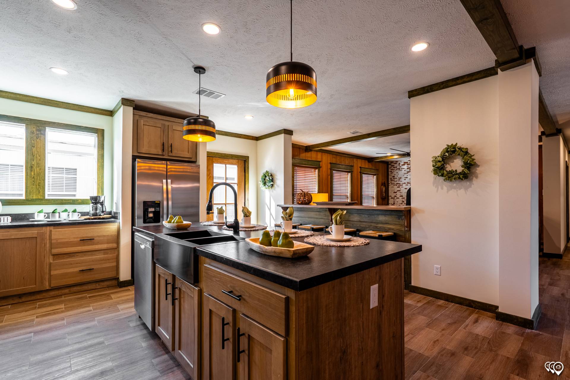 A modern kitchen with wooden cabinets, a black island, and stainless steel appliances. Warm lighting and green accents create a cozy, inviting atmosphere.