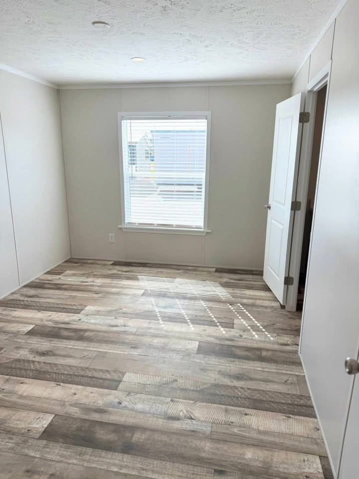 Bright, empty room with light wood flooring, white walls, and a window with blinds. Sunlight casts shadows on the floor, creating a calm atmosphere.