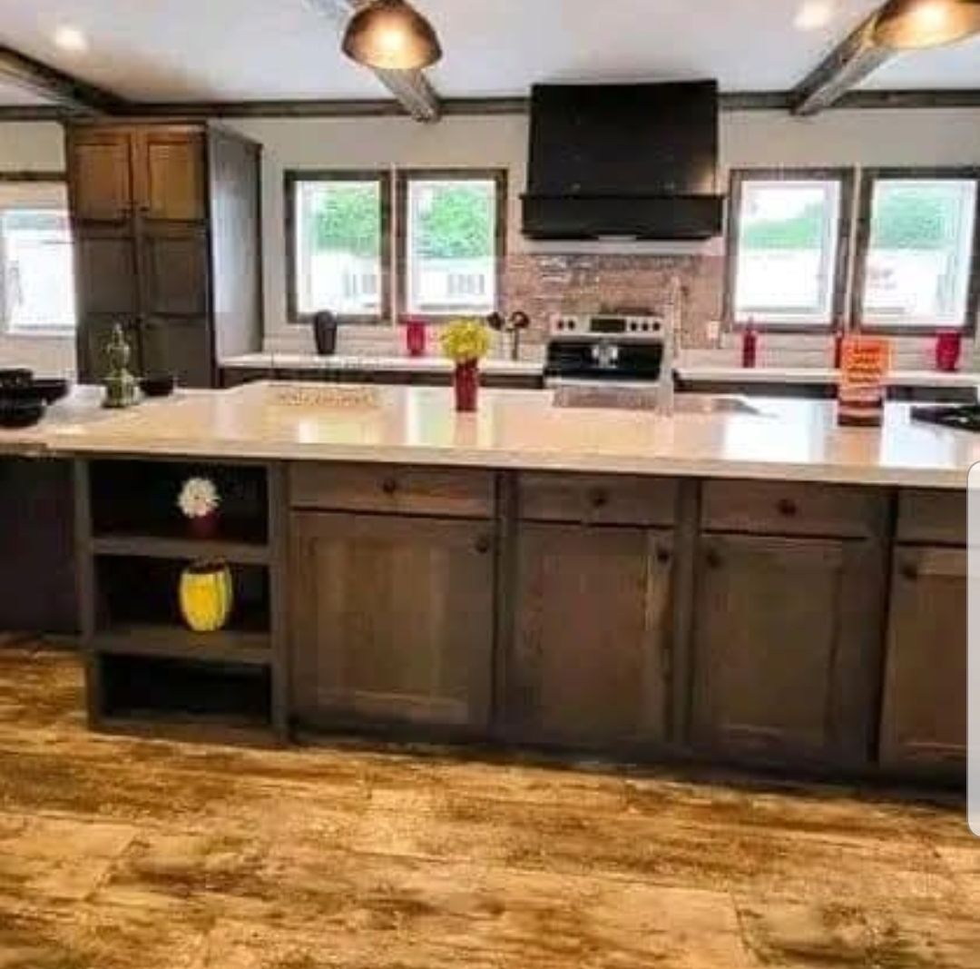 Spacious kitchen with wood cabinets and a large island with a white countertop. Bright windows light the space, creating a warm and inviting atmosphere.