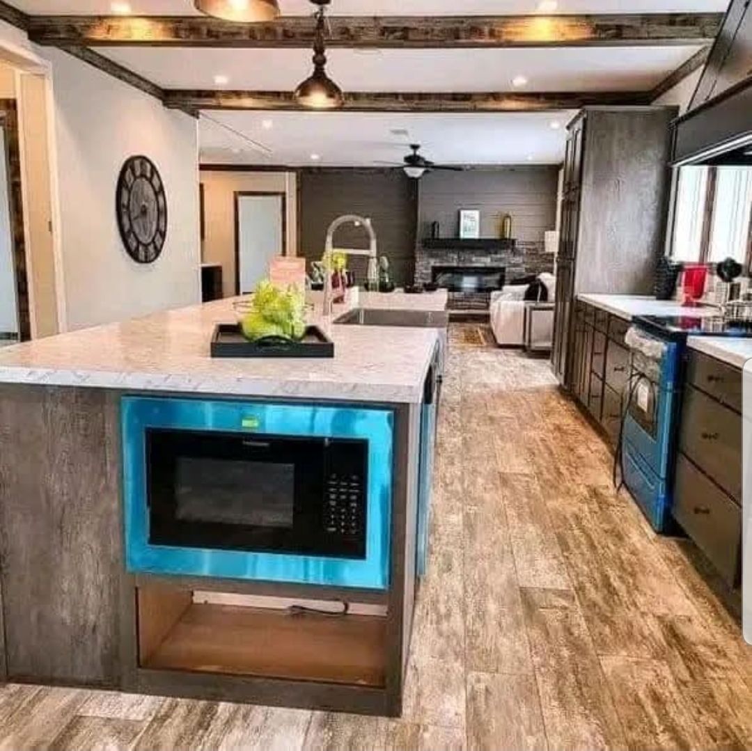 Modern kitchen with a rustic touch features a large island with a built-in microwave. Wooden beams, sleek countertops, and cozy living area in view.