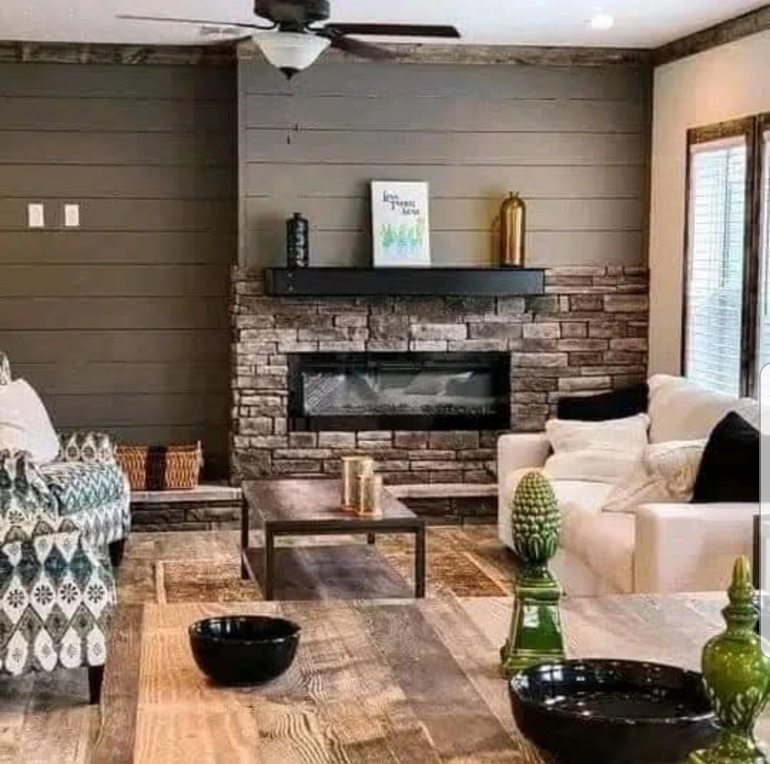 Modern living room with a stone fireplace, wooden paneling, and cozy white sofas. A coffee table and decorative items create a warm, inviting atmosphere.