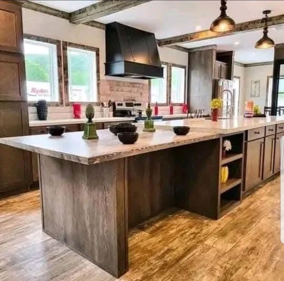 Spacious kitchen with wooden cabinets and island, marble countertop, pendant lights, and decorative items. Bright and modern with a warm tone.