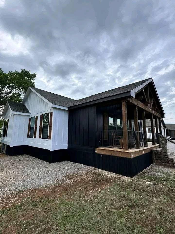 Modern house exterior with contrasting white and dark panels, large windows, and a porch with wooden beams under a cloudy sky. Peaceful and inviting.