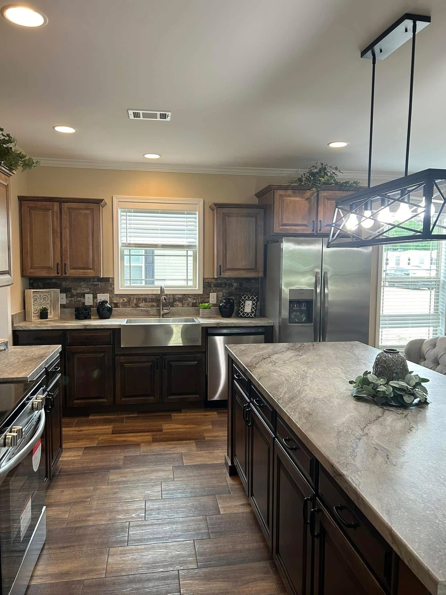 Modern kitchen with dark wood cabinets, stainless steel appliances, and a central island. Bright overhead lighting and a window add natural light.