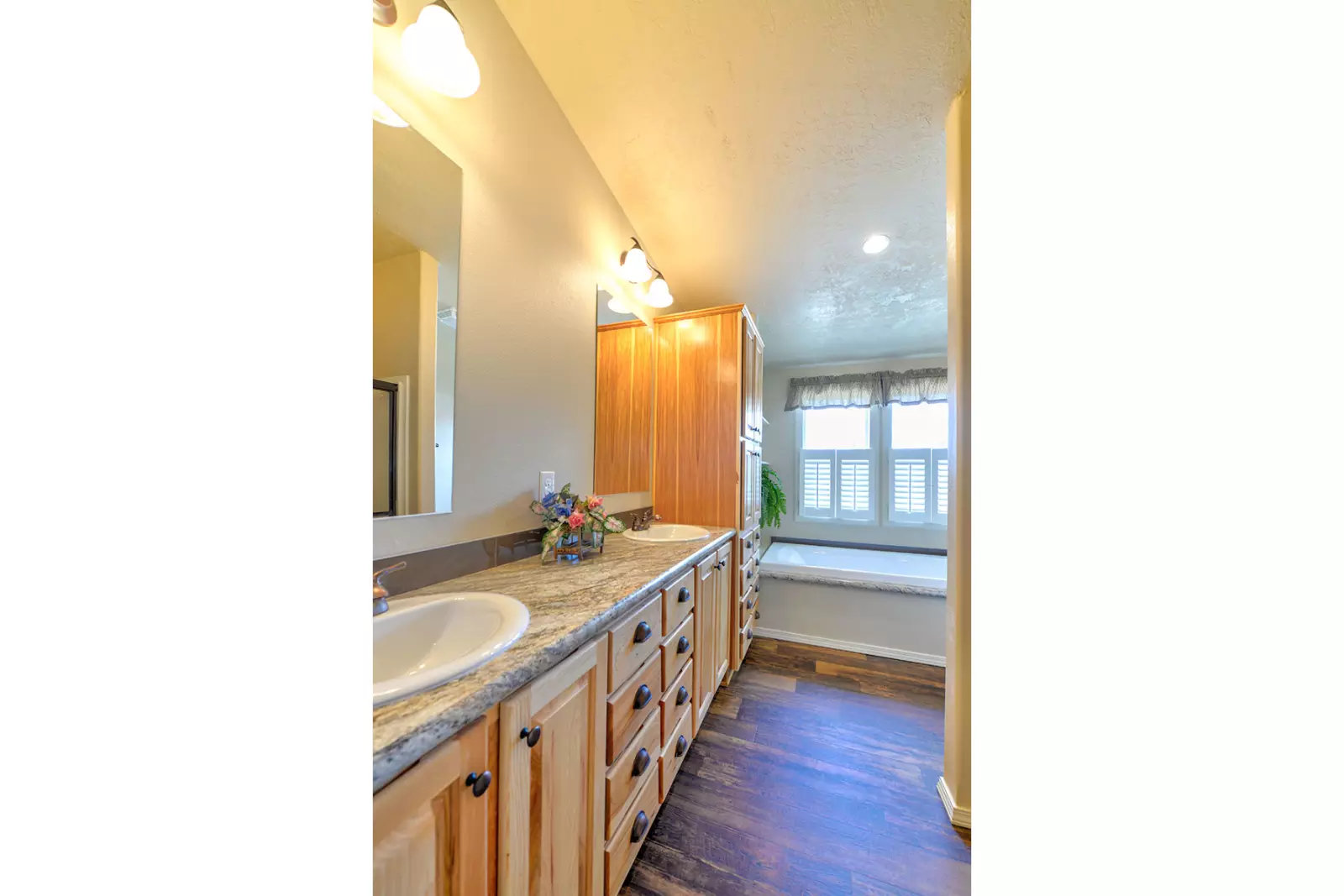 Bright bathroom with wooden cabinets, marble countertop, and a white sink. Window with white shutters and bench seat. Cozy and inviting ambiance.