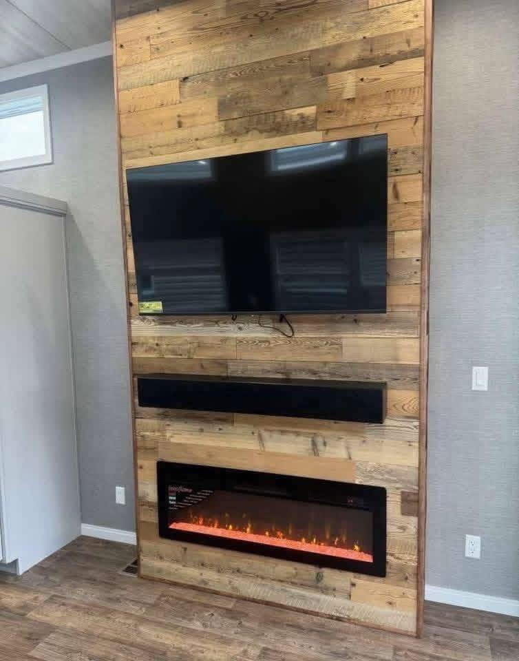 Wall-mounted TV and fireplace with a modern, rustic design. The wooden wall features a large flat-screen TV, black soundbar, and sleek electric fireplace.