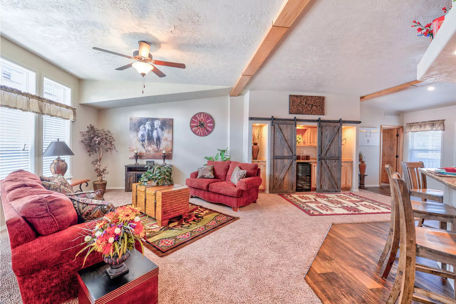 Cozy living room with a warm palette. Features red sofas, rustic barn doors, and wooden furniture. Soft lighting and plants add a welcoming ambiance.
