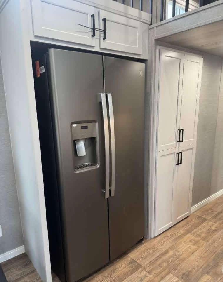 Stainless steel side-by-side refrigerator with a water dispenser, nestled between white cabinets. The kitchen has a modern, sleek design.