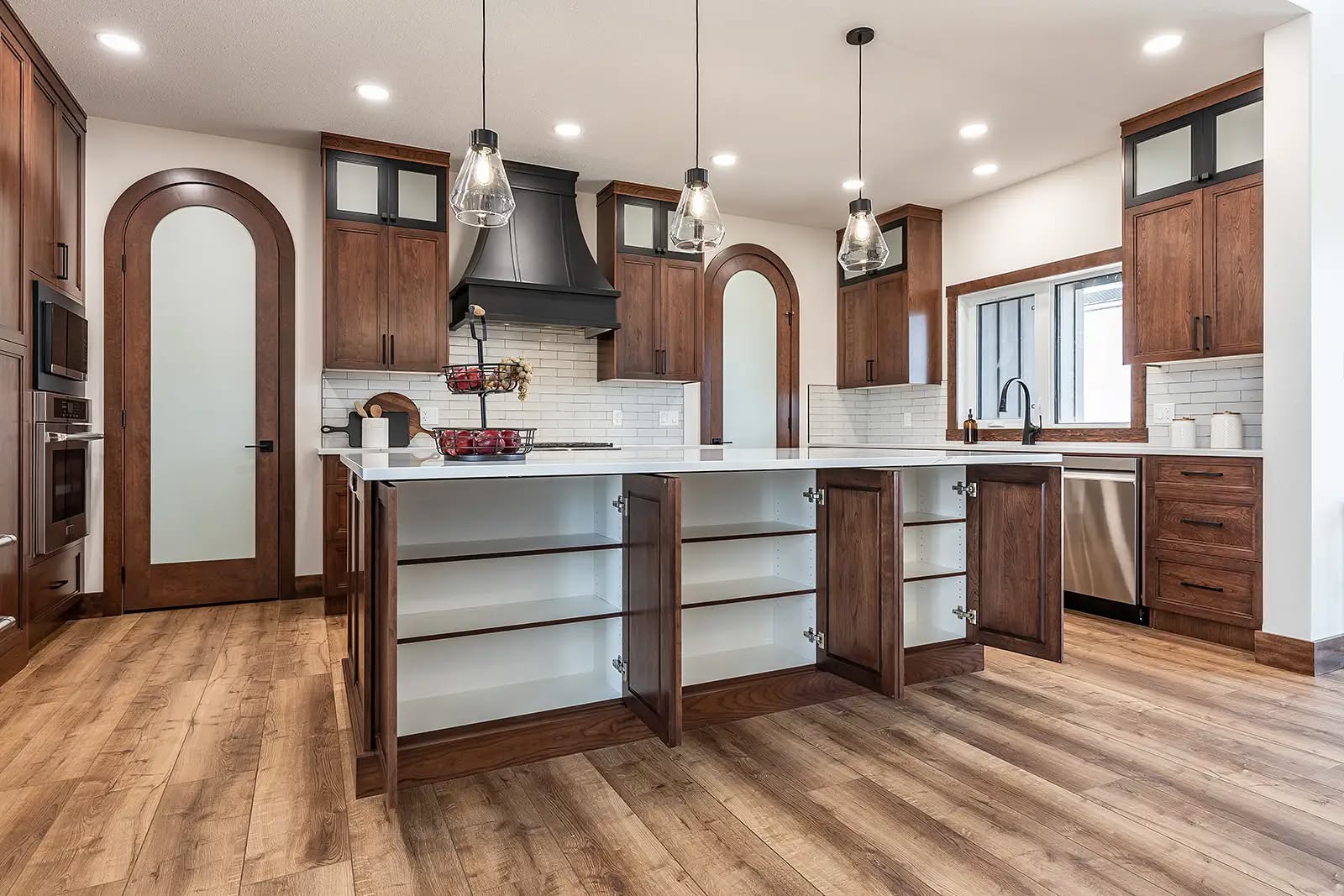 Spacious kitchen with open wooden cabinets, white countertops, and stainless steel appliances. Pendant lights hang above the island, creating a modern, warm ambiance.