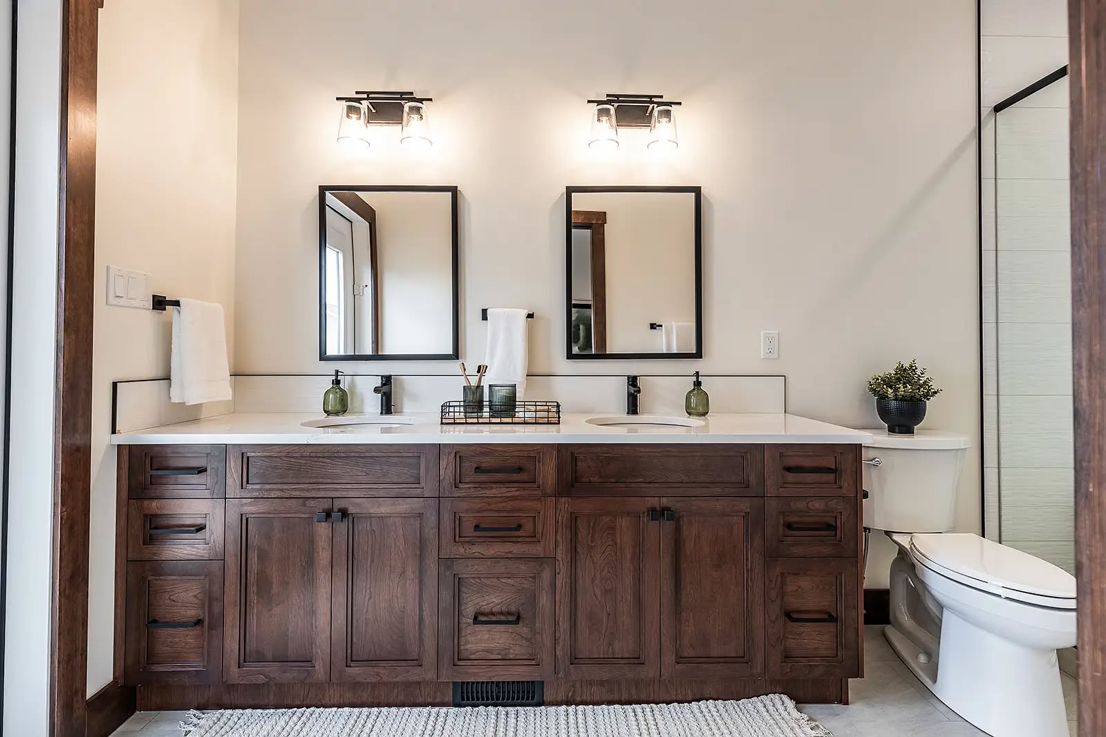 Modern bathroom with a two-sink vanity featuring dark wood cabinets, two mirrors, and soft lighting. Neutral tones create a calm and elegant ambiance.