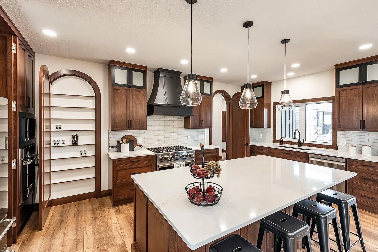 Spacious kitchen with warm wooden cabinets, arched shelving, and a large white island. Pendant lights hang overhead, creating a welcoming atmosphere.