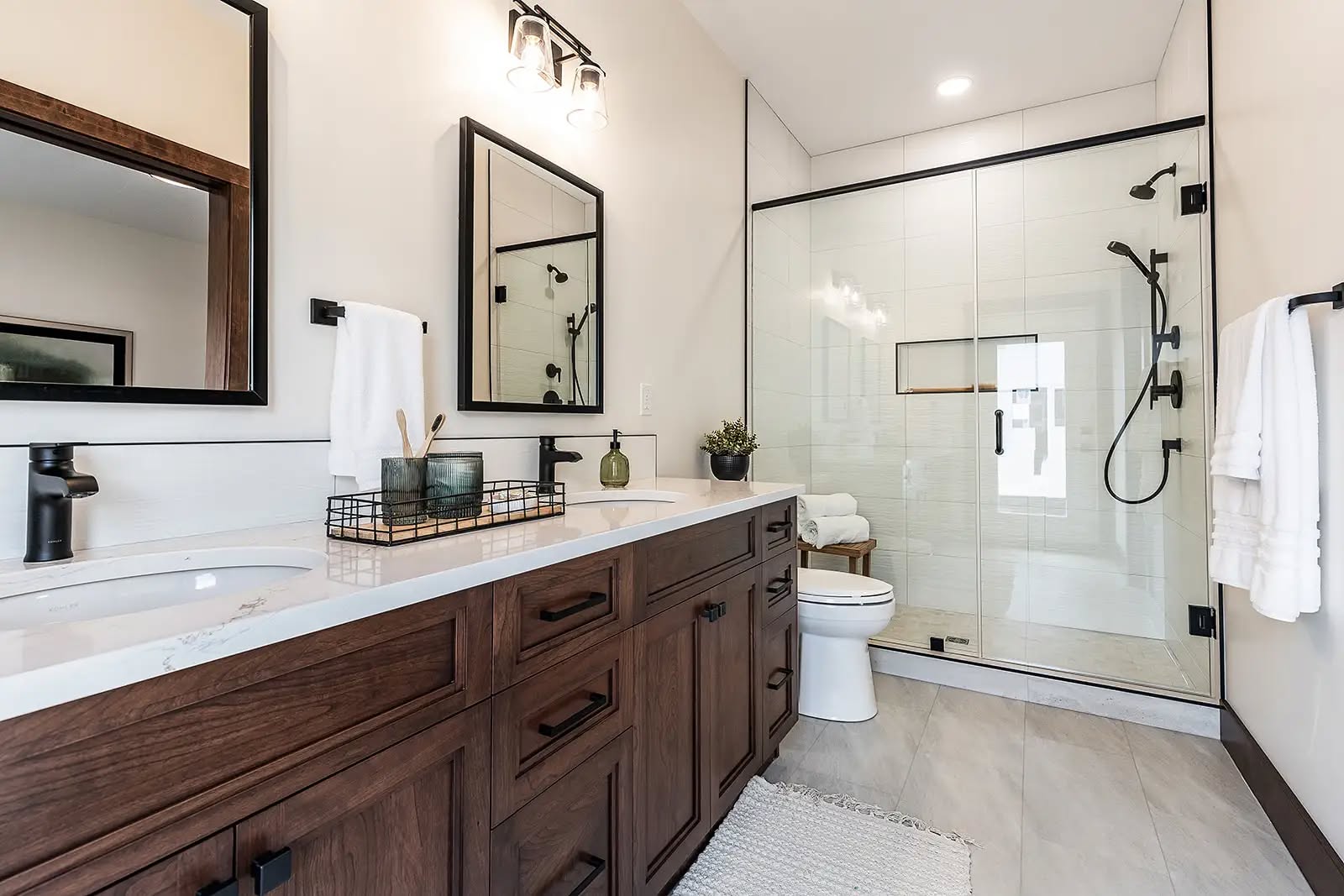 Modern bathroom with a wooden vanity, twin sinks, and black-framed mirrors. Glass shower, potted plant, and neutral tones create a serene vibe.