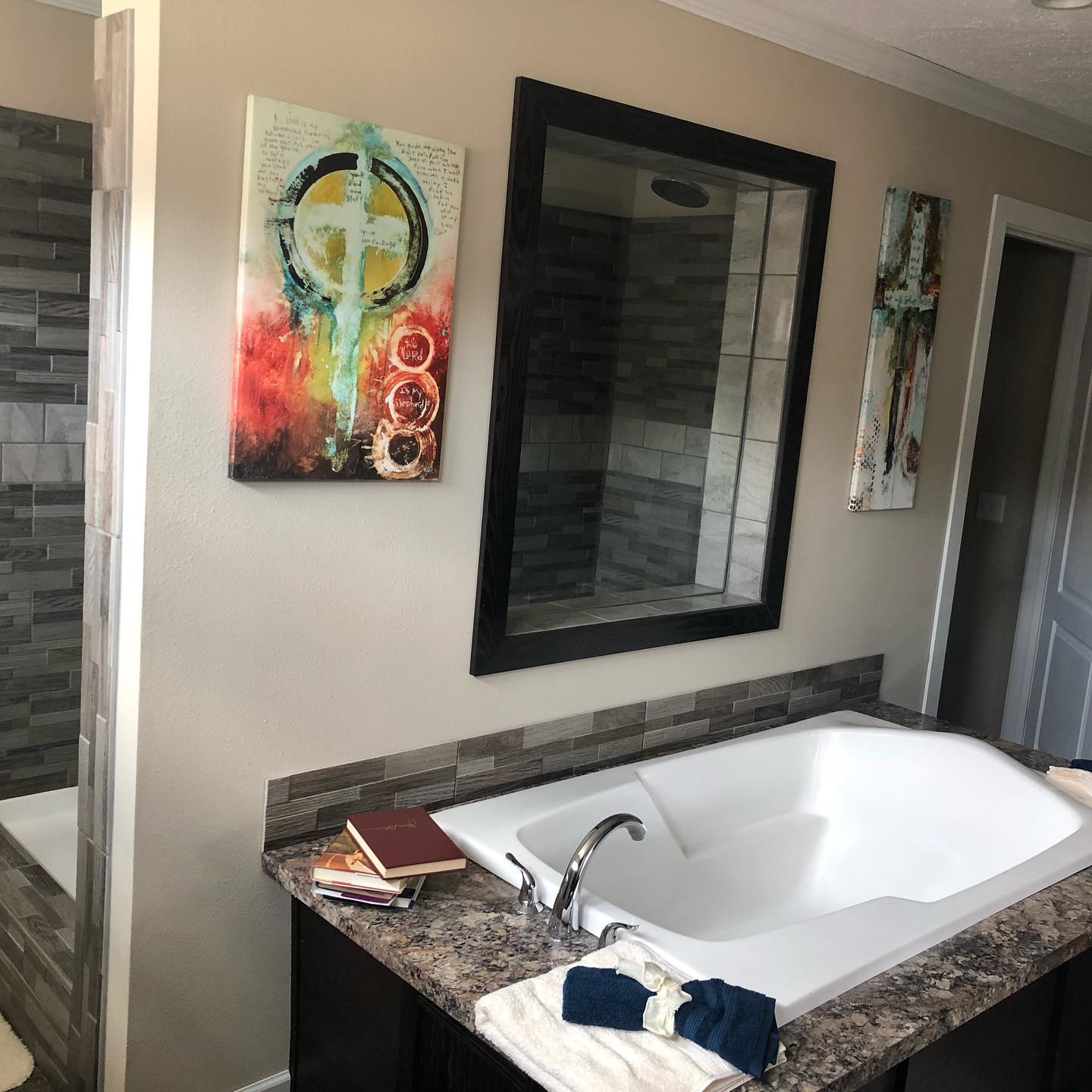 Modern bathroom with a large white bathtub, marble countertop, abstract art, and towels; warm tones create a calming atmosphere.
