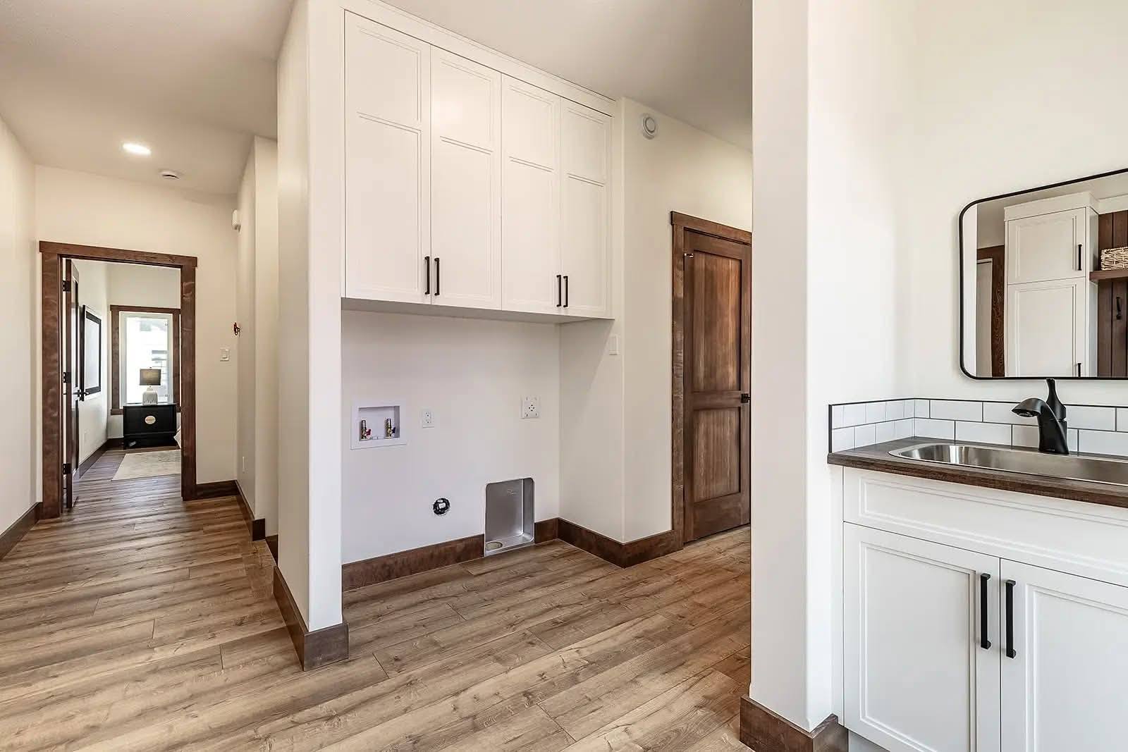 Spacious laundry room with light wood flooring, white cabinets, and a built-in sink. Neutral tones create a clean, organized, and modern feel.