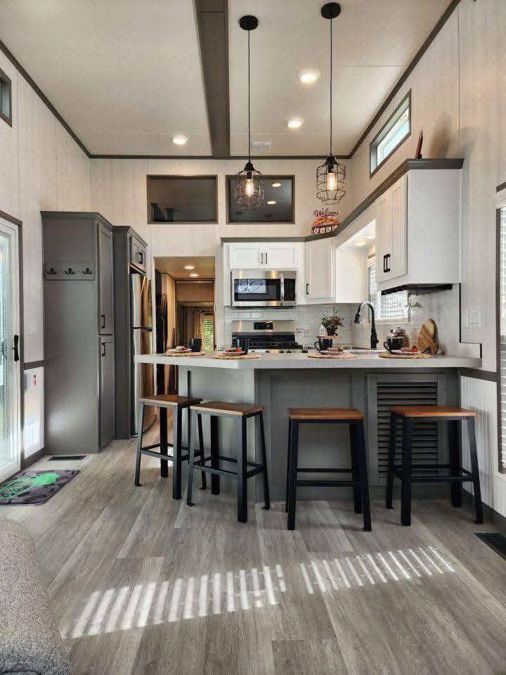Modern kitchen with white cabinets, gray accents, and wood flooring. Features a central island with stools, pendant lights, and sleek appliances. Cozy and inviting atmosphere.
