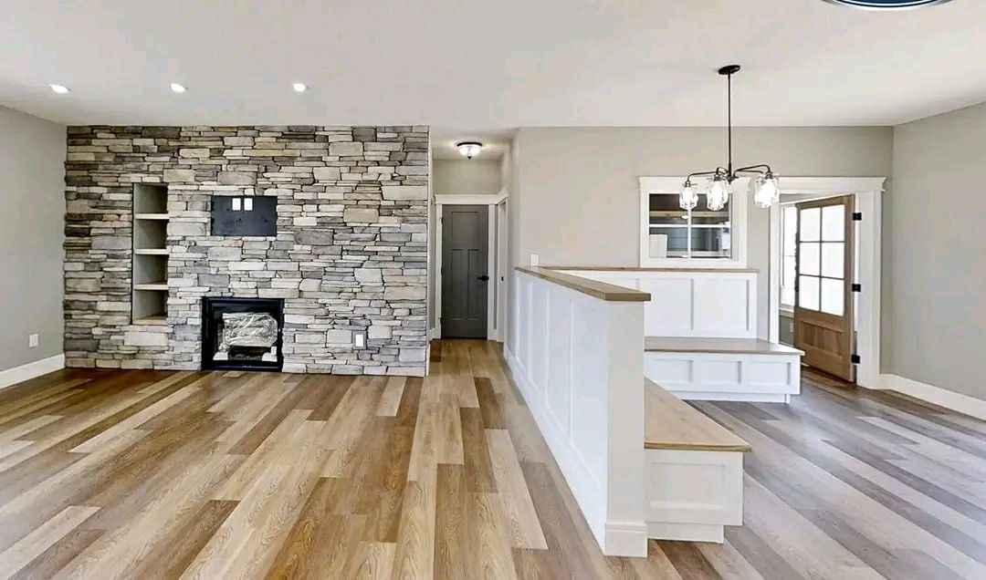 Modern living room with a stone accent wall featuring a built-in fireplace and shelves. Light wood flooring, neutral gray walls, and a chandelier create a cozy ambiance.